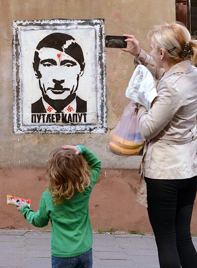 Eine Frau fotografiert ein Poster von Waldimir Putin mit Hitler-Seitenscheitel und -Schnauzbart in der westukrainischen Stadt Lviv.