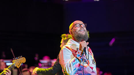 Der Fronts&auml;nger der oberbayerischen Band Dreiviertelblut Sebastian Horn. Hinter ihm dirigiert Gregor Mayrhofer die M&uuml;nchner Symphoniker, die am Dienstagabend mit der Band genre&uuml;bergreifend musizieren.