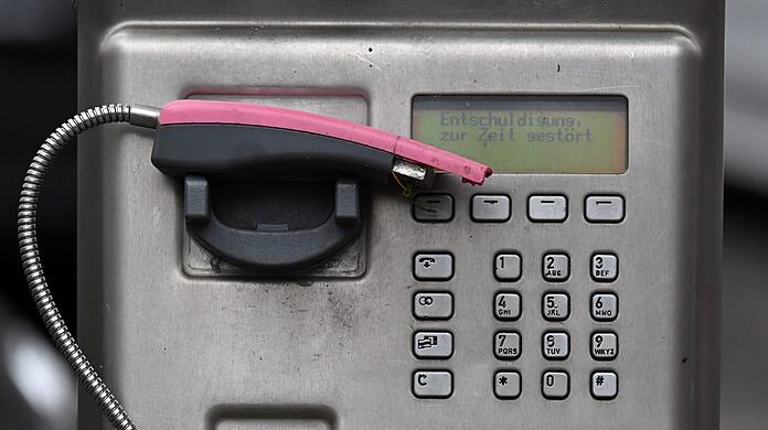 Ein abgebrochener Telefonhörer liegt in der Halterung eines deaktivierten Fernsprechers.