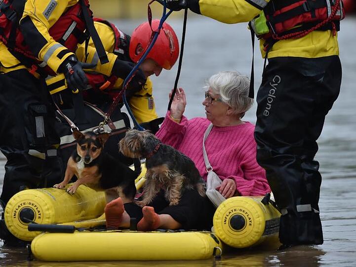 Rettungskräfte bringen eine Frau und ihre Hunde mit einem Schlauchboot in Sicherheit.