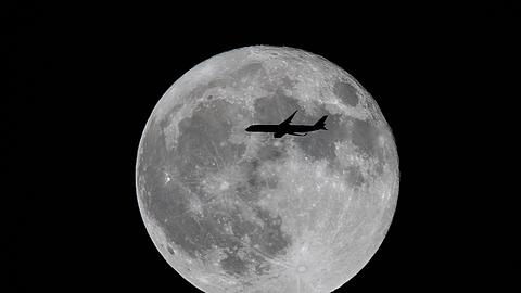 Ein Flugzeug fliegt an einem gro&szlig;en Vollmond vorbei.