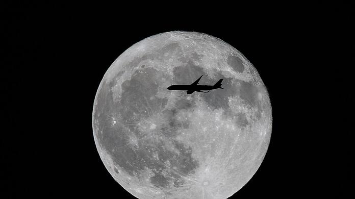 Ein Flugzeug fliegt an einem großen Vollmond vorbei.