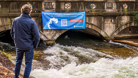 Mit einem großen Banner wirbt "Die Bayerische" an der Eisbachwelle für ihr Gewinnspiel.