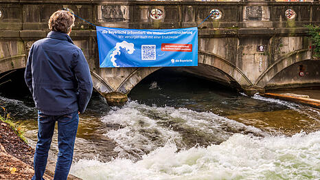 Mit einem großen Banner wirbt "Die Bayerische" an der Eisbachwelle für ihr Gewinnspiel.