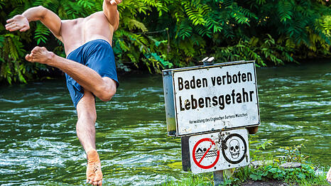 "Baden Verboten - Lebensgefahr" steht auf einem Schild am Ufer. Ein Mann springt trotzdem in den Eisbach im Englischer Garten.