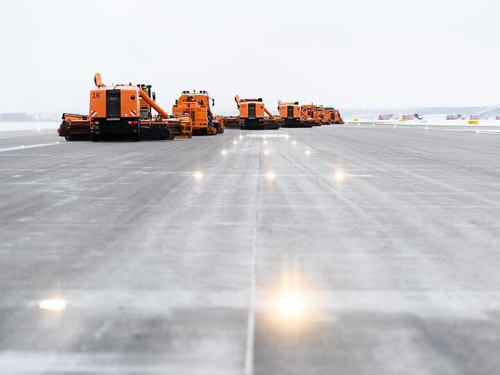 Zahlreiche versetzt fahrende Räumfahrzeuge mit Schneeschaufeln befreien die Startbahn am Flughafen vom Schnee. Foto: Matthias Balk/Archiv