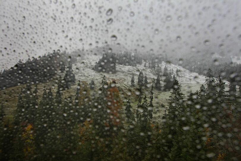 Hinter der regennassen Fensterscheibe einer Gondel der Nebelhornbahn liegt am 15.10.2012 die teilweise mit Schnee bedeckte herbstliche Landschaft bei Oberstdorf (Bayern).