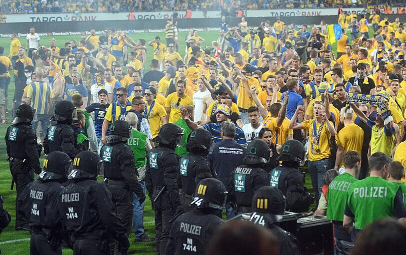 Braunschweiger Fans stehen Polizisten und Ordnern nach dem Abpfiff auf dem Platz gegenüber.