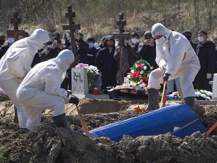 Totengräber in Schutzkleidung lassen auf einem Friedhof im russischen Kolpino den Sarg eines Covid-19-Opfers in ein Grab hinab.