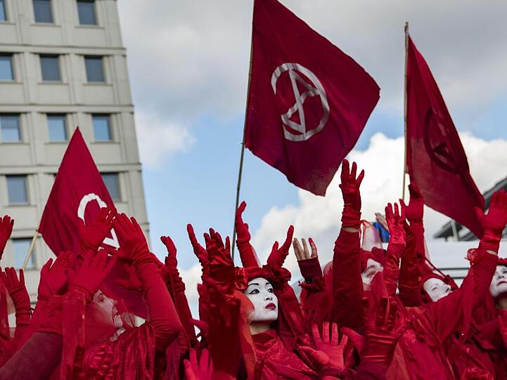 Aktivisten von Extinction Rebellion gehen in roten Gewändern und mit weiß angemalten Gesichtern über den Potsdamer Platz in Berlin.