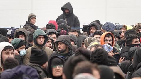 Migranten warten vor einer Lagerhalle in der Nähe der Grenze.