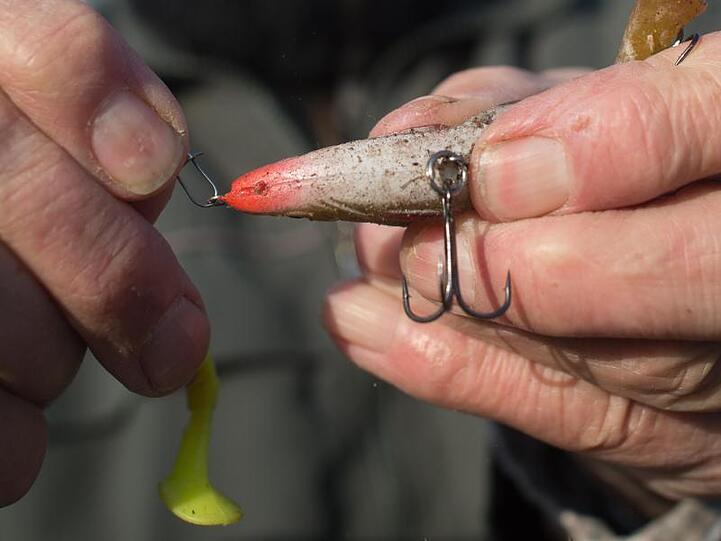 Ein Angler bereitet seine Angel vor und hängt einen Drilling an die Angelschnur. Der Fischereiverband beschäftigt sich derzeit mit dem Kliamwandel.