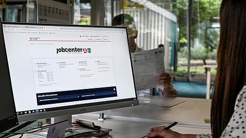 Eine Mitarbeiterin eines Jobcenters sitzt am Computer und spricht mit einem Antragsteller (Symbolbild).