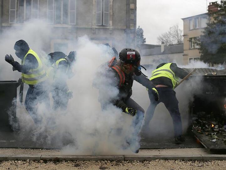 Teilnehmer einer Demonstration der "Gelbwesten" gehen in Bourges hinter ihren Barrikaden in Deckung, als Polizisten Tränengas einsetzen.