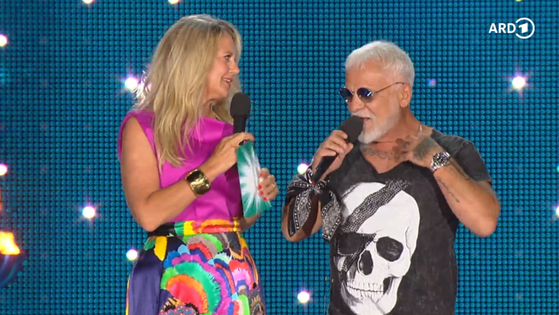 Barbara Schöneberger zog bei der "Starnacht am Wörthersee" 2025 Nino de Angelos Shirt herunter, um sein Brust-Tattoo zu lesen. Barbara Schöneberger zog bei der "Starnacht am Wörthersee" 2025 Nino de Angelos Shirt herunter, um sein Brust-Tattoo zu lesen.