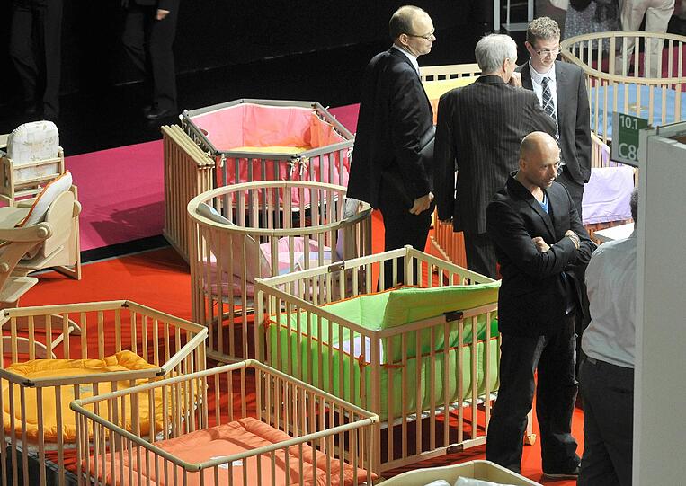 Besucher stehen bei der Messe der Baby- und Kleinkindausstattungsbranche "Kind+Jugend" in Köln zwischen Laufställen.