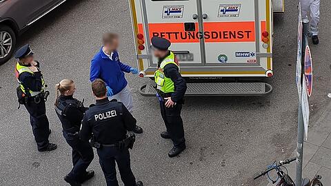 Vier Polizisten stehen hinter einem Rettungsdienst (Symbolbild)