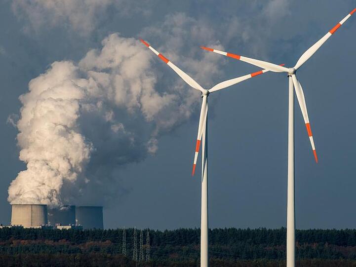 Windräder drehen sich vor den Kühltürmen des Braunkohlekraftwerkes in Jänschwalde (Brandenburg).