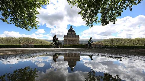 Was für ein Kunstwerk im Hofgarten: Staatskanzlei, Radler, Wolken und blauer Himmel spiegeln sich in einer Pfütze.
