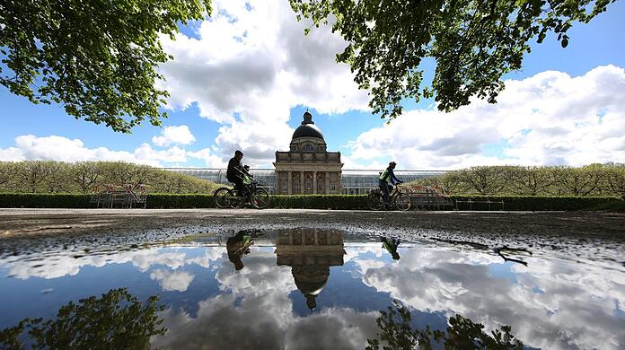 Was für ein Kunstwerk im Hofgarten: Staatskanzlei, Radler, Wolken und blauer Himmel spiegeln sich in einer Pfütze.