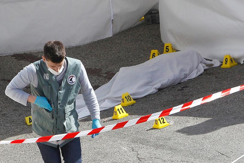 Ein Forensiker untersucht den Tatort. Im Hintergrund die zugedeckte Leiche eines der beiden Todesopfer.