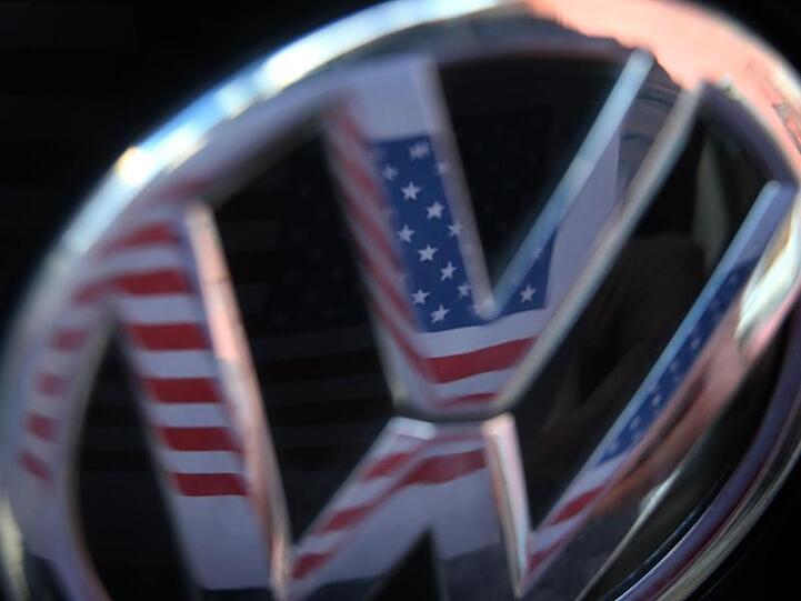 Eine US-Flagge spiegelt sich im Logo eines Volkswagens.