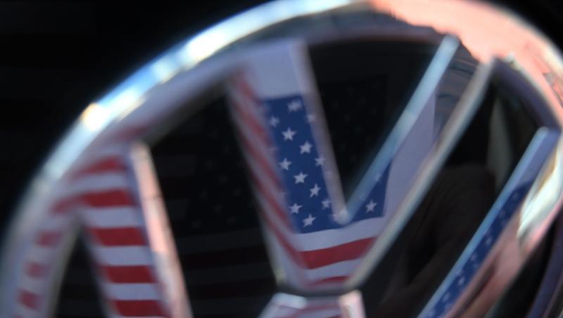 Eine US-Flagge spiegelt sich im Logo eines Volkswagens. Eine US-Flagge spiegelt sich im Logo eines Volkswagens.