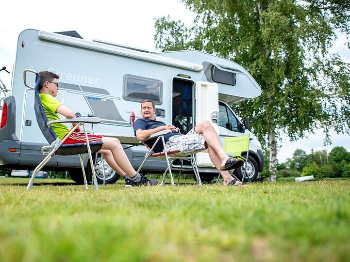 Ein Mann und ein Kind sitzen vor ihrem Wohnmobil. Foto: Hauke-Christian Dittrich/dpa/Symbolbild