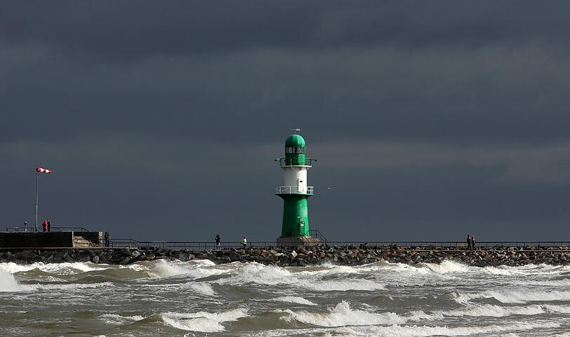 Im Ostseebad Rostock-Warnemünde (Mecklenburg-Vorpommern) sind am 30.03.2015 Spaziergänger an der Mole am aufgewühlten Wasser unterwegs, während sich am Himmel dunkle Sturmwolken und Sonne abwechseln.