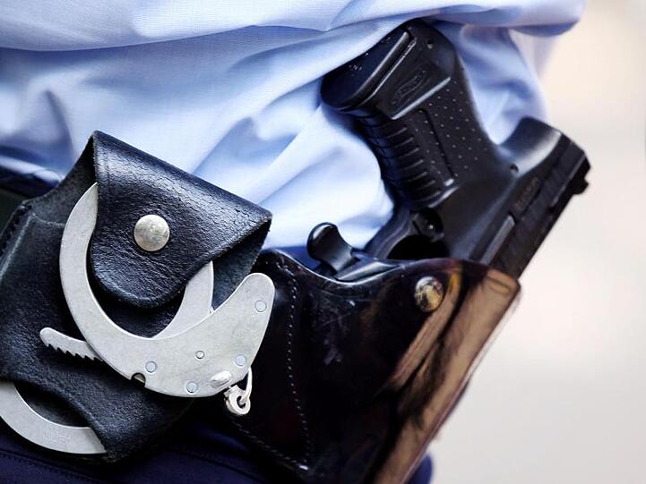 Ein Polizist mit Handschellen und Pistole am Gürtel. Foto: Oliver Berg/dpa/Archivbild