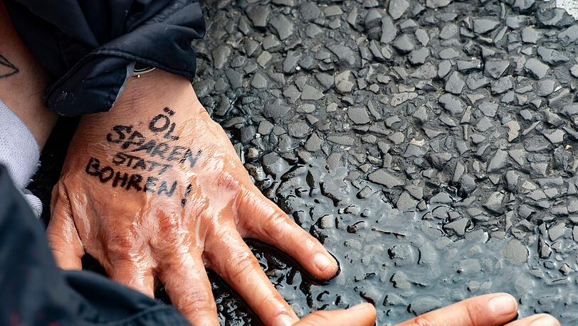 "Öl sparen statt bohren" steht auf der Hand einer Demonstrantin der Gruppe "Letzte Generation", die sich auf dem Asphalt festgeklebt hat.