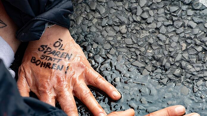 "Öl sparen statt bohren" steht auf der Hand einer Demonstrantin der Gruppe "Letzte Generation", die sich auf dem Asphalt festgeklebt hat.