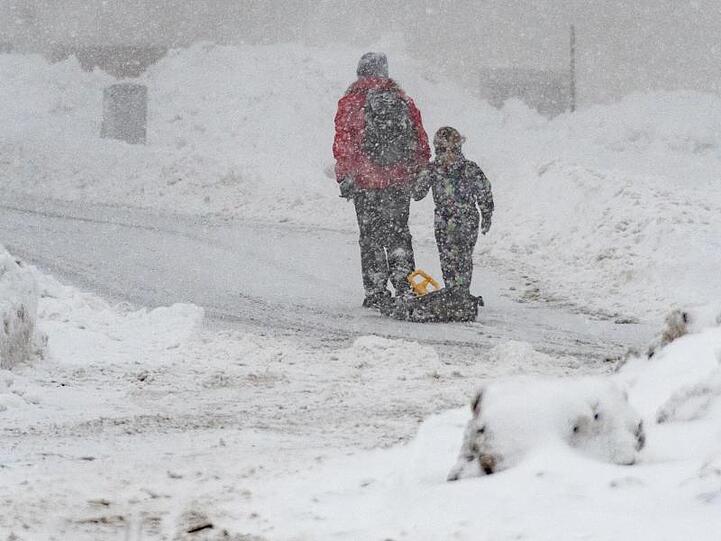 Eine Frau und ein Kind gehen mit einem Schlitten auf einer verschneiten Straße in Sankt Englmar. Foto: Armin Weigel/Archiv