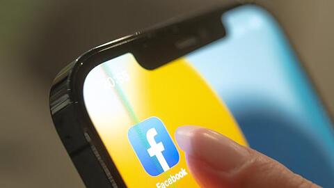 Eine Frau hält ihr Handy in der Hand, auf dem die Facebook-App zu sehen ist.).