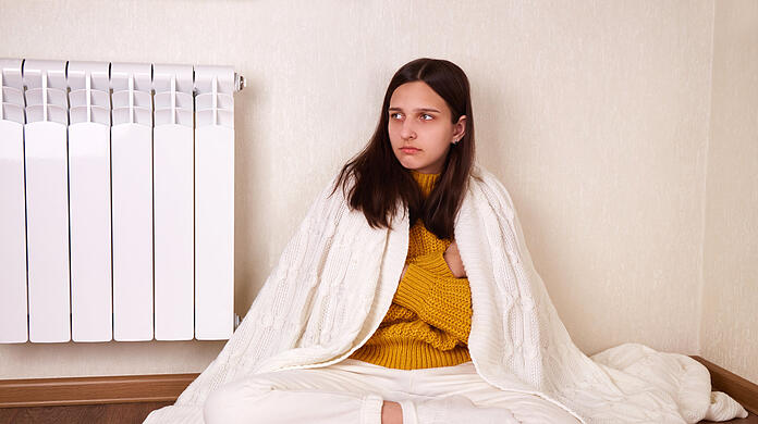 Eine Frau friert, weil die eigene Wohnung nicht angemessen geheizt werden kann. Wegen schlechter Isolierung oder zu teuren Energiepreisen.