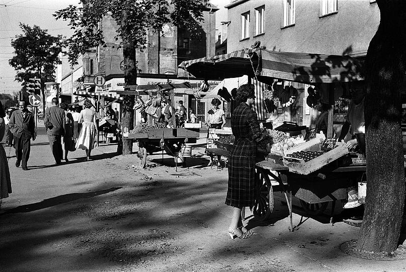 Wo heute Cafés, Bars und Autos das Straßenbild prägen, flaniert man 1957 noch gemütlicher &ndash; und auch
improvisierter: Die östliche Seite der Leopoldstraße, Ecke Nikolaistraße mit Blick gen Norden.