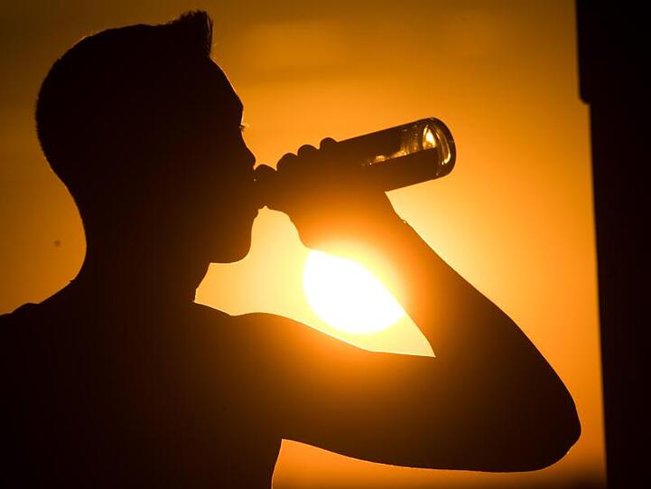 Ein Mann trinkt vor der untergehenden Sonne aus einer Flasche. Foto: Julian Stratenschulte/dpa/Symbolbild