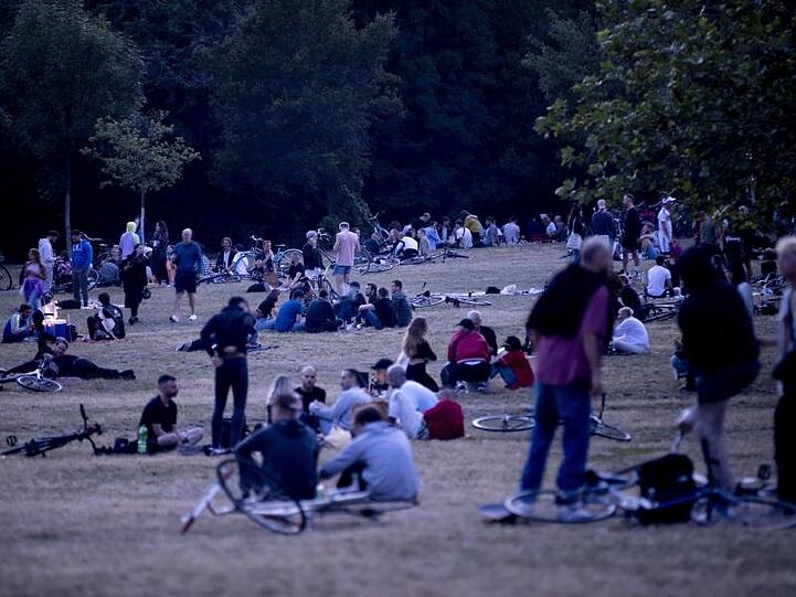 Menschen sitzen nachts im Volkspark Hasenheide auf einer Wiese.