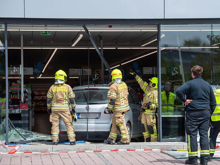 Feuerwehrmänner schneiden ein Auto aus der Glasfront eines Supermarkts. Foto: Lino Mirgeler