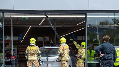 Feuerwehrmänner schneiden ein Auto aus der Glasfront eines Supermarkts. Foto: Lino Mirgeler