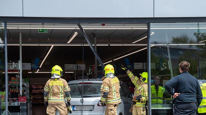 Feuerwehrmänner schneiden ein Auto aus der Glasfront eines Supermarkts. Foto: Lino Mirgeler