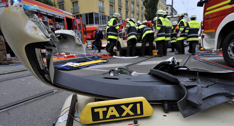 Vorne im Bild liegt das Dach des Taxis auf dem Boden. Im Hintergrund kümmern sich die Hilfskräfte um den schwer verletzten Taxler...