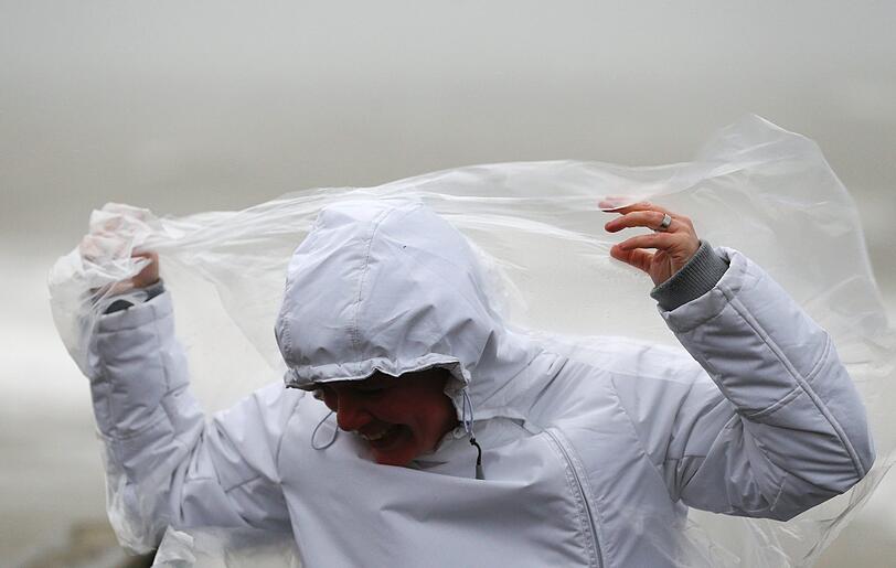Eine Frau versucht in Wenningstedt auf Sylt ihr Regencape festzuhalten - der Wind hat etwas dagegen.