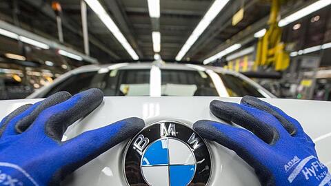 Ein Mitarbeiter montiert im BMW-Werk ein BMW-Emblem auf den Kofferraumdeckel eines Fahrzeugs der 7er Reihe. Foto: Armin Weigel/Archiv