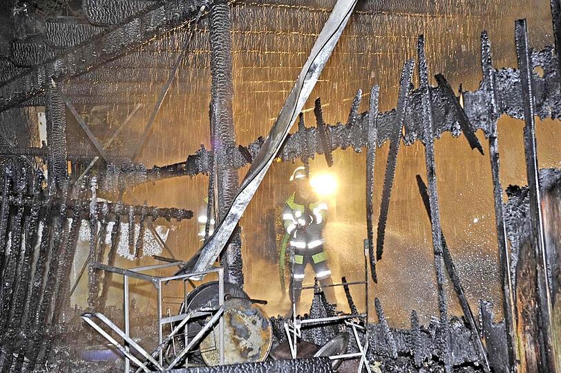 Ein Feuerwehrmann steht in dem völlig zerstörten Holzbau.