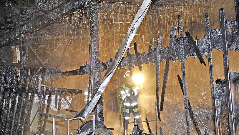 Ein Feuerwehrmann steht in dem völlig zerstörten Holzbau.