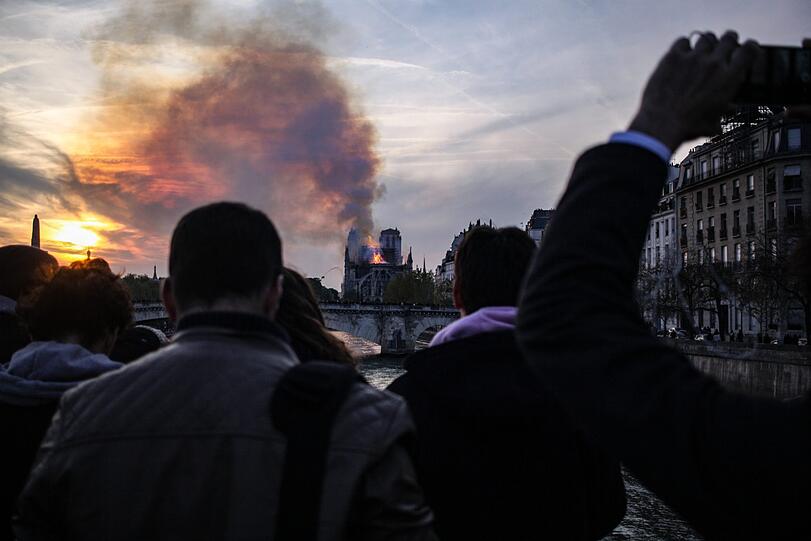 Die weltberühmte Kathedrale Notre-Dame de Paris steht in Flammen. Schaulustige haben sich am Ufer der Seine versammelt.