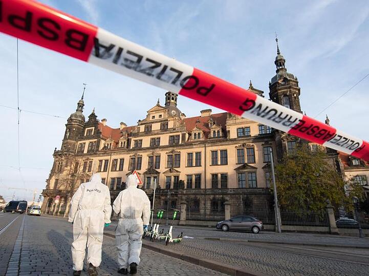 Zwei Mitarbeiter der Spurensicherung stehen vor dem Residenzschloss mit dem Grünen Gewölbe hinter einem Absperrband.