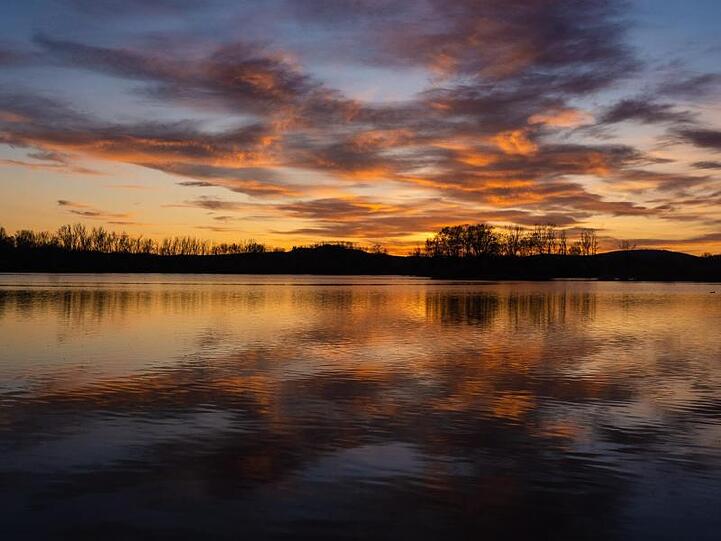 Der bunte Abendhimmel spiegelt sich im Wasser des Baggersees von Breitengüßbach. Foto: Nicolas Armer/dpa/Archivbild