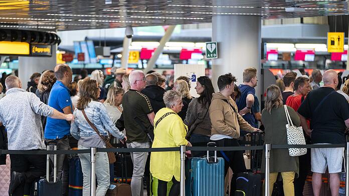 Reisende stehen in der Abflughalle des Amsterdamer Flughafens Schiphol Schlange.